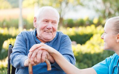 Senior in rolstoel krijgt hand van verpleger